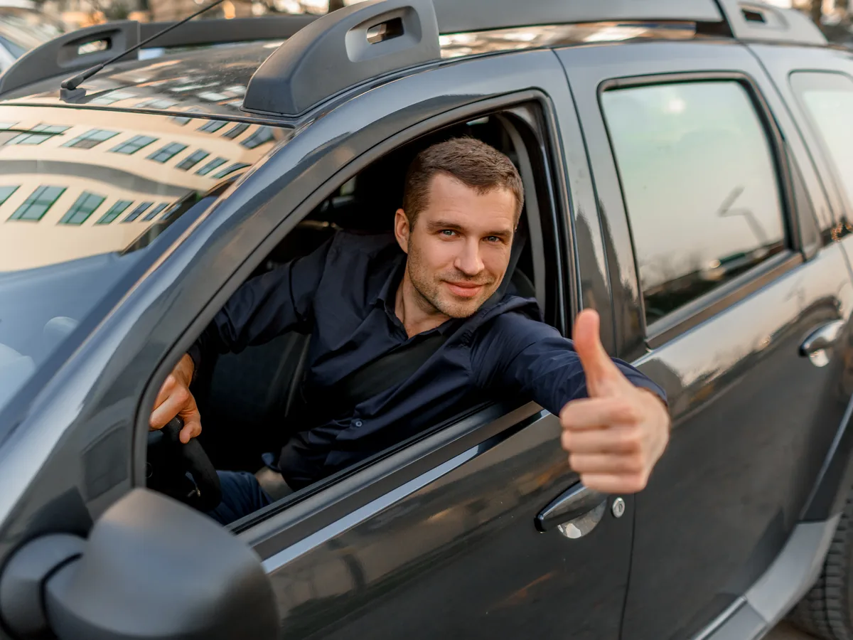 Mann am Steuer eines Autos, Daumen nach oben aus dem Seitenfenster